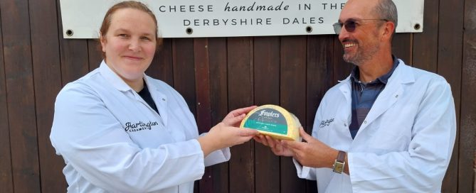 Hartington creamery workers holding half a wheel of cheese